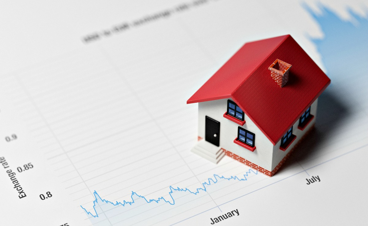 Small red-roofed house model placed on a financial chart showing housing market trends from January to July.