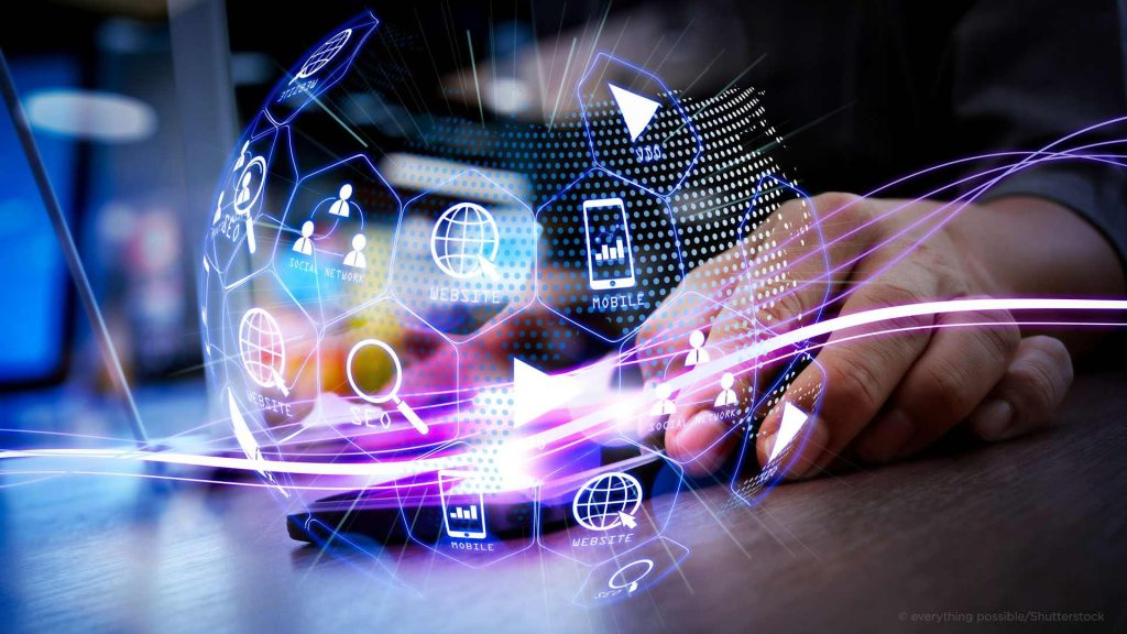 Hands interacting with a glowing holographic network of icons and light trails above a desk surface.